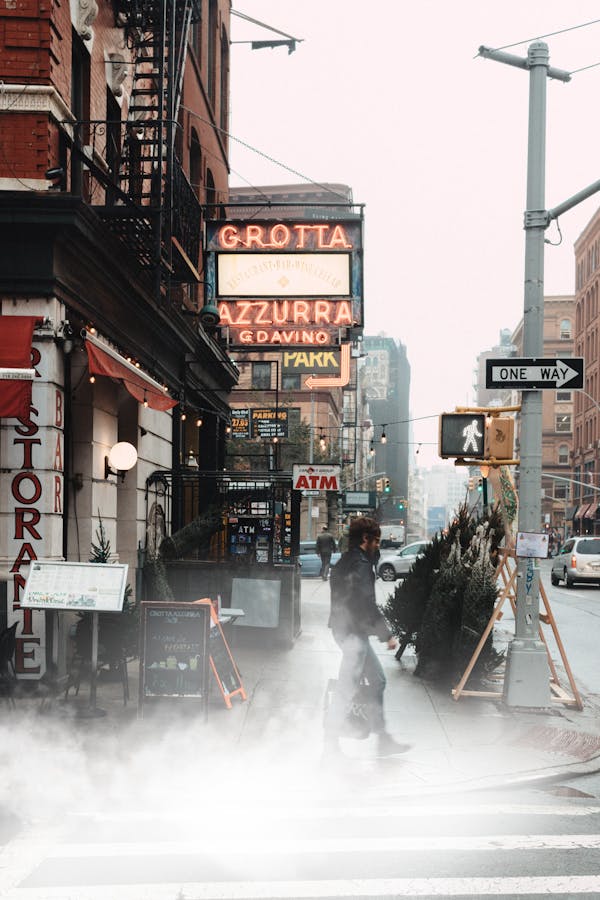 A man crosses a foggy street in New York City, surrounded by urban architecture and signs.