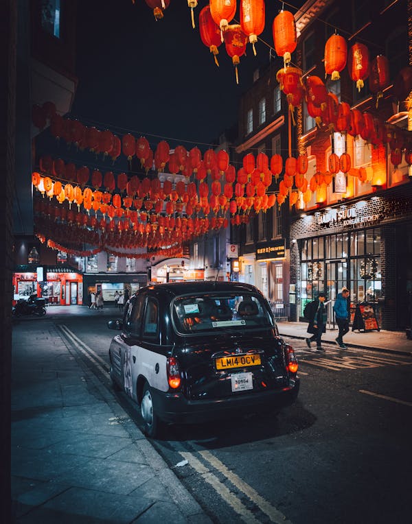 A vibrant night scene in London's Chinatown featuring red lanterns and a black cab.