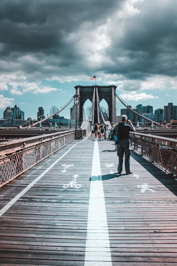 Iconic view of Brooklyn Bridge filled with pedestrians under dramatic skies.