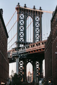 Old suspension bridge with massive arch under cloudless clear sky in contemporary city