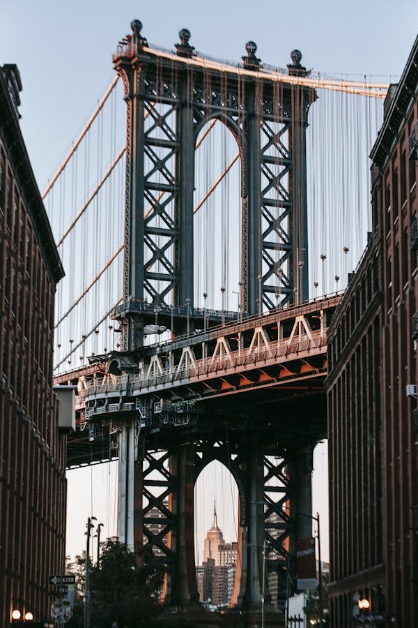 Old suspension bridge with massive arch under cloudless clear sky in contemporary city