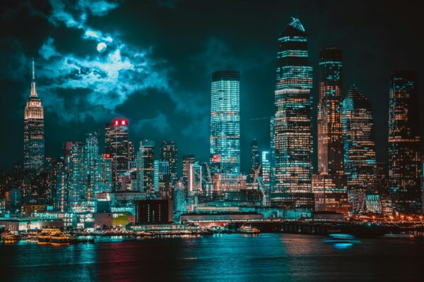 Stunning view of New York City skyline with illuminated skyscrapers and reflections on water at night.