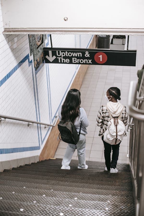 Two women with backpacks enter a subway in New York City, following safety protocols.