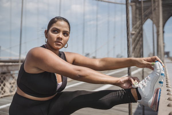 Woman stretching on Brooklyn Bridge, preparing for workout in sunny weather.