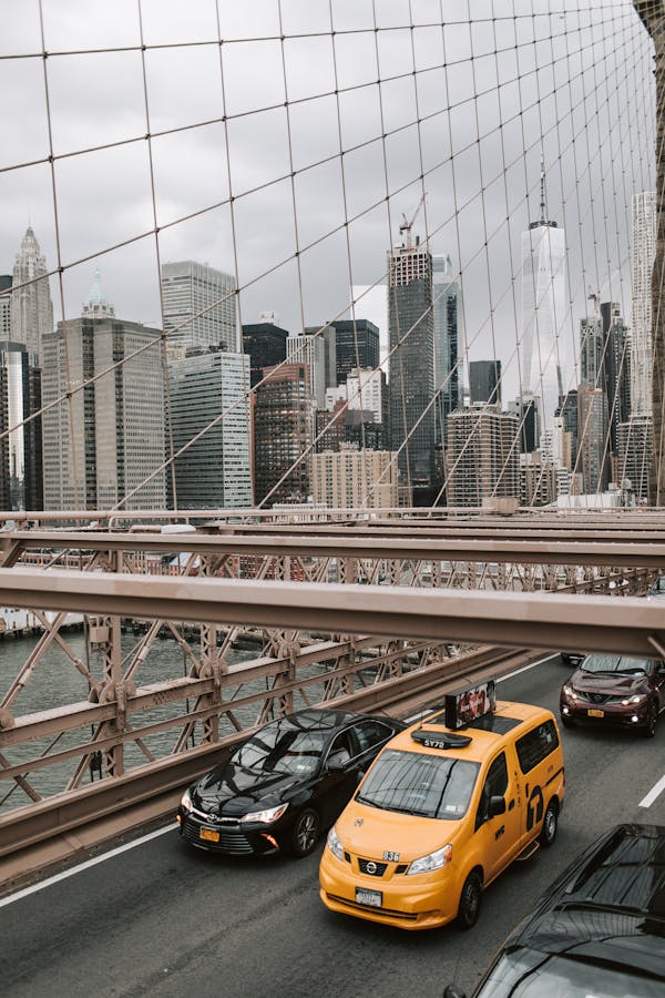 Yellow taxi crossing Brooklyn Bridge with Manhattan skyline in view.
